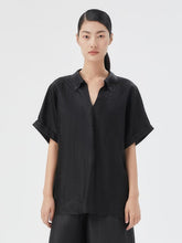 A lady wears a silk shirt and black shorts.